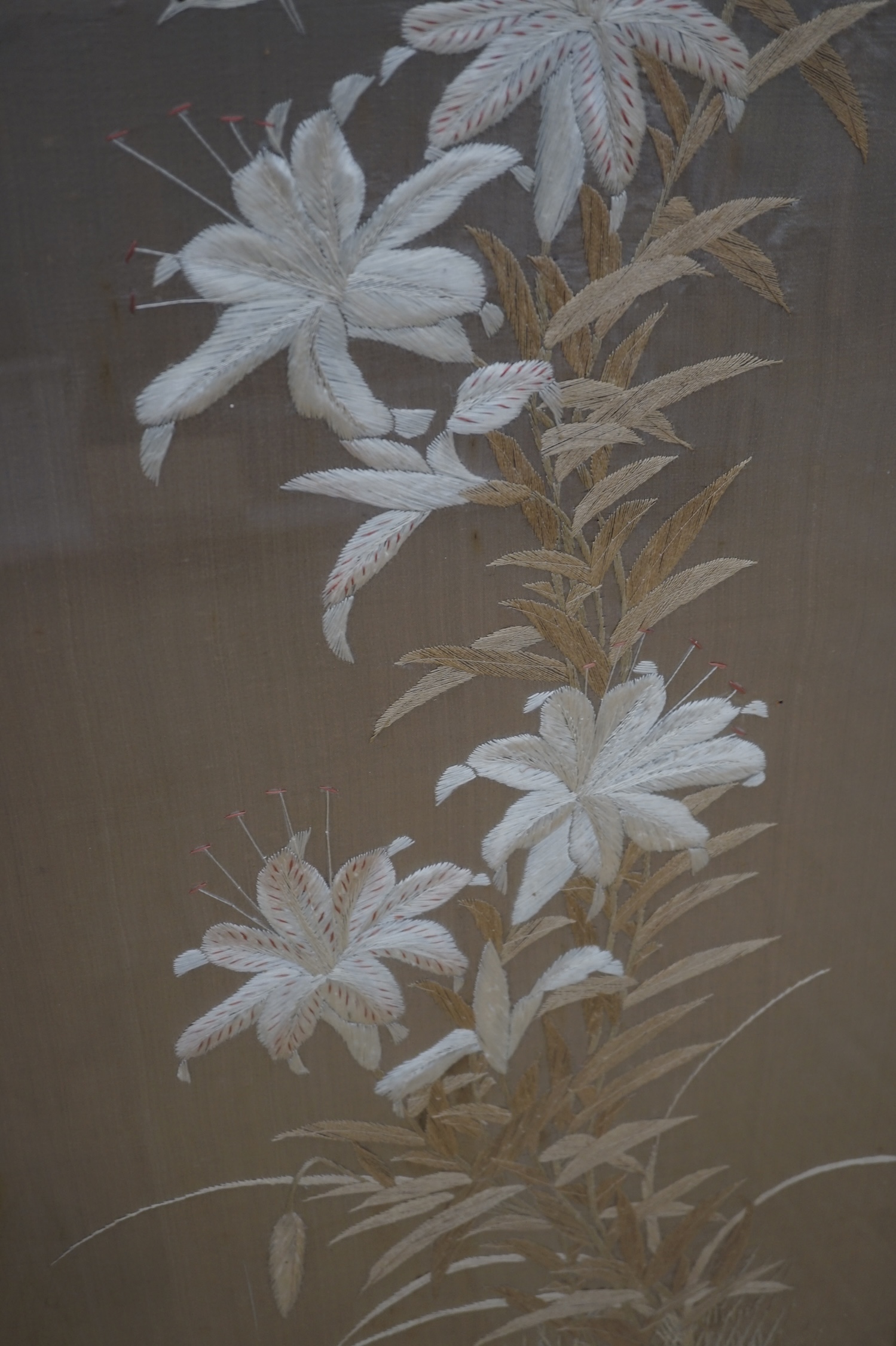 A 1900 to 1920’s Japanese silk embroidery of birds in flight and flowers on a grey background, 131cm high, 52cm wide, together with a Japanese silk and metallic thread still life embroidery on black background, with couc